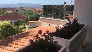 A balcony with a glass railing overlooking a cityscape, a tiled roof, and potted plants. - Villa Nunzia (Ercolano)