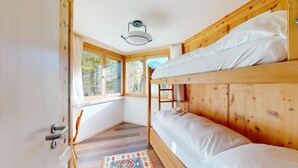 Una habitación con literas, paredes de madera, una ventana con cortinas, una puerta con manija y una lámpara en el techo.