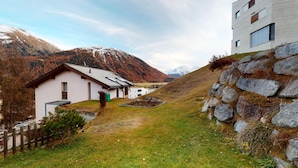 Un entorno rural con una casa blanca, un muro de piedra y montañas al fondo.