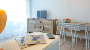En moderne stue med et fjernsyn på et træskab, et spisebord med stole, og et magasin på bordet.