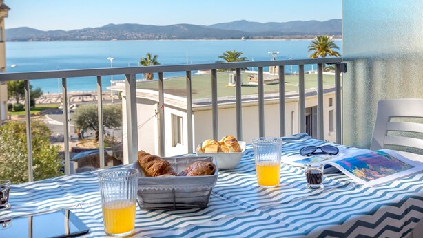 En balkon med et bord dækket til morgenmad, med udsigt over kysten.