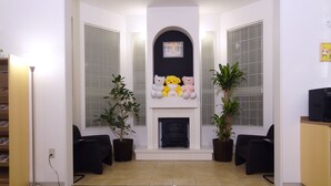 A living room with a fireplace, two potted plants, a black sofa, and a bookshelf. - Family Lodge Hatagoya Kisarazukou (Kisarazu)