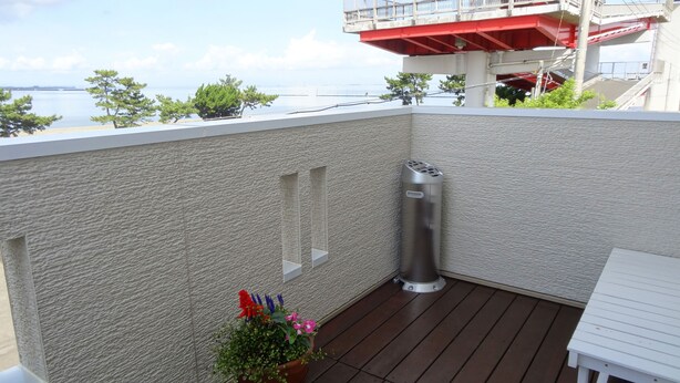 A balcony with a textured wall, a metal trash can, and a small potted plant with flowers. - Family Lodge Hatagoya Kisarazukou (Kisarazu)