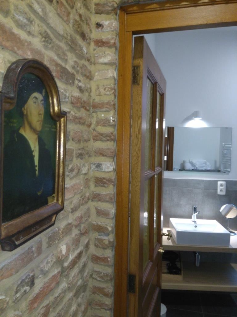 Een badkamer met een houten deur, een wastafel, een spiegel en een ingelijst beeld aan de muur.