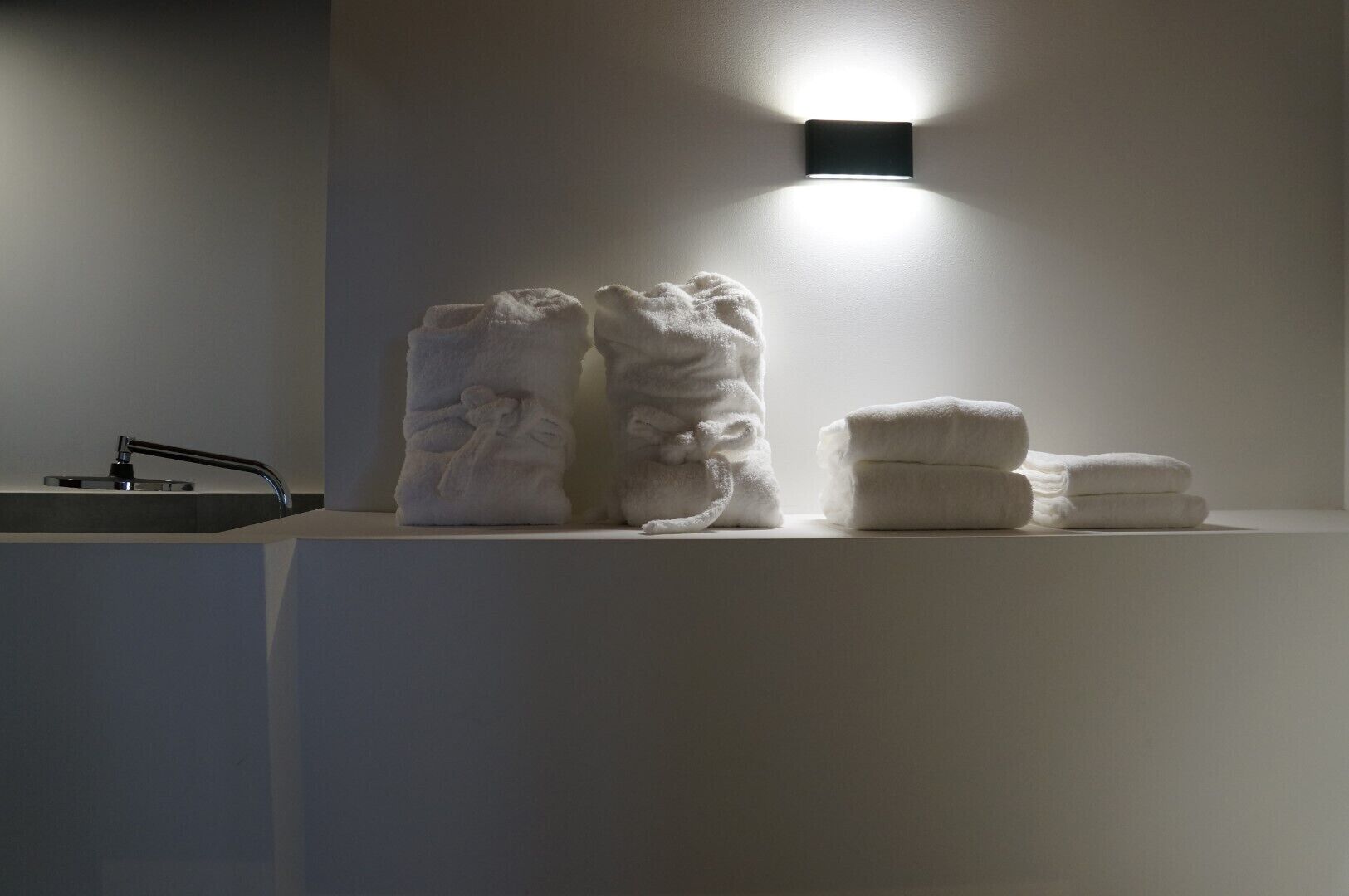 Een badkamer met een wastafel, een lampje aan de muur en handdoeken op een plank.