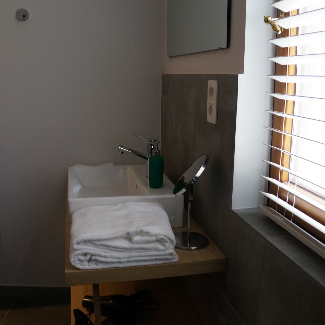 A bathroom with a bathtub, a towel, a green soap dispenser, and a mirror.