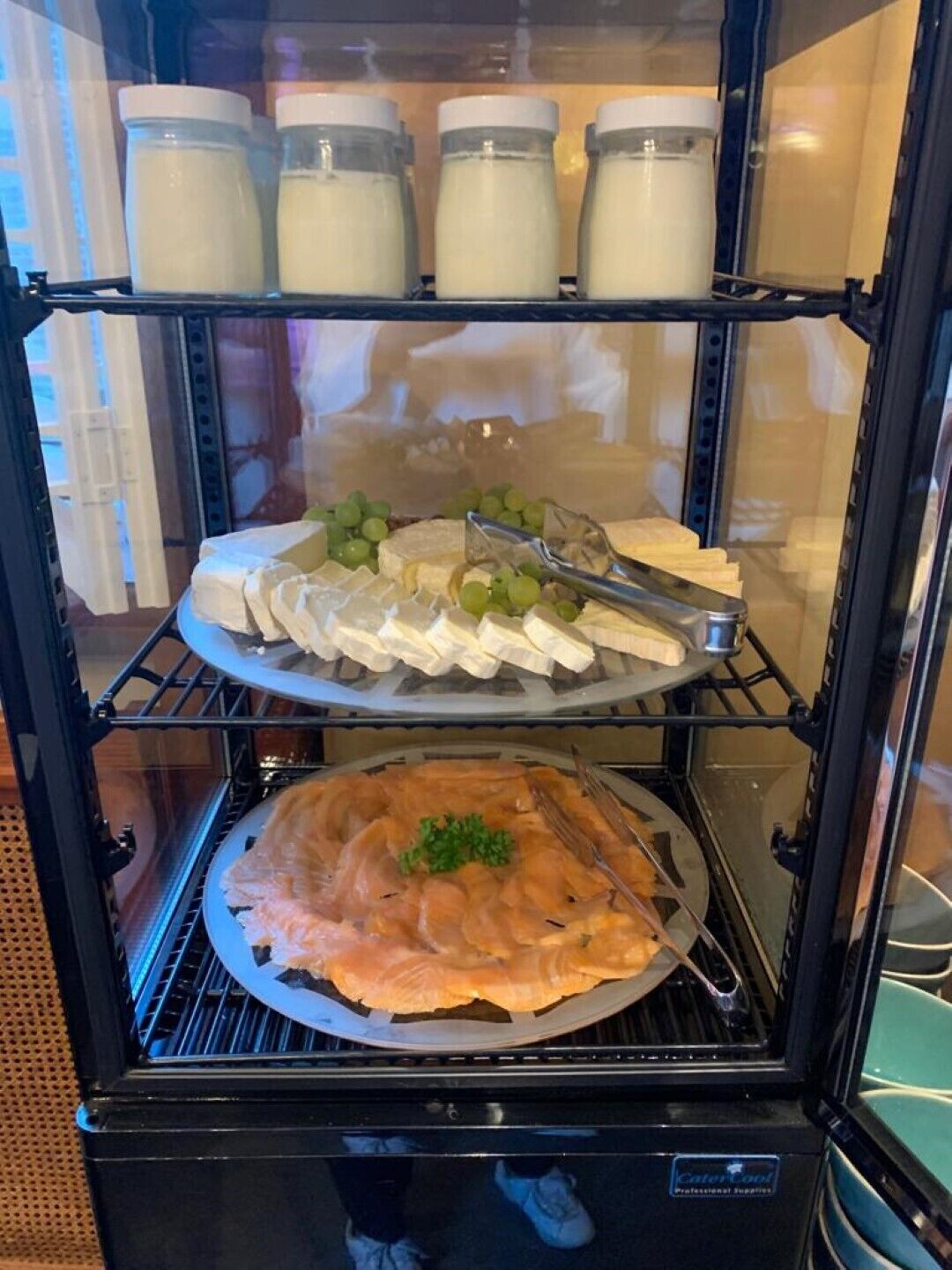 A food display case with various cheeses, grapes, and a salmon dish.