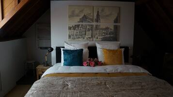 Une chambre à coucher avec un lit, une table de chevet, une lampe et un mur orné de deux tableaux encadrés.