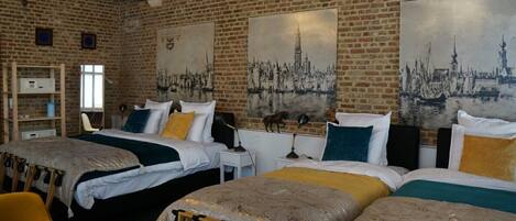 A hotel room with three beds, a brick wall, and two large cityscape paintings.