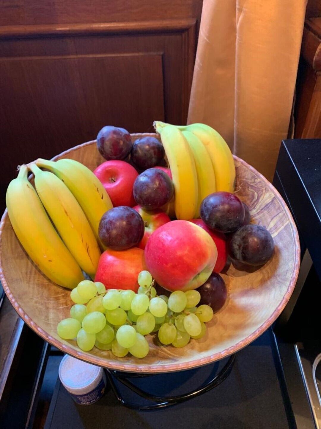 Een houten schaal vol bananen, appels, pruimen en druiven.