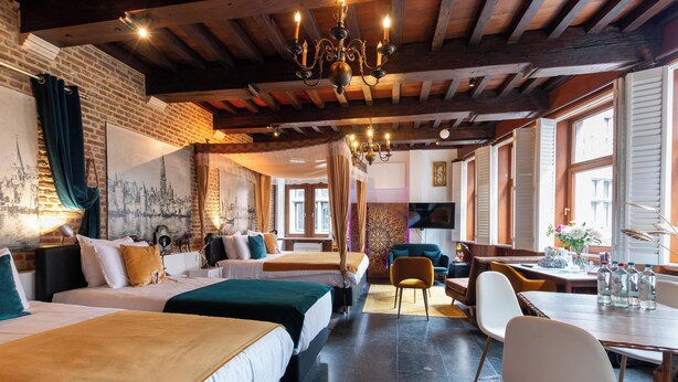 Una habitación de hotel con tres camas, una mesa de comedor y un candelabro.