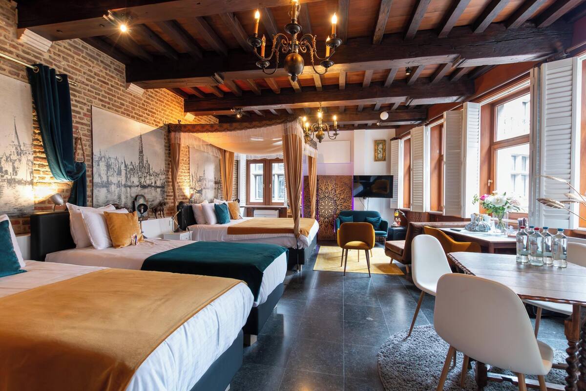 A hotel room with three beds, a dining table, and a chandelier.
