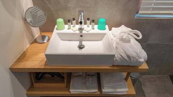 A bathroom sink with toiletries, a mirror, and towels on a wooden shelf.