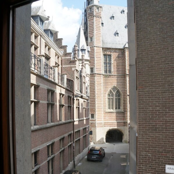 A narrow alleyway with a brick building featuring a large arched window and a turret. A car is parked in front of the building. - Charming Suites Jan Zonder Vrees (Antwerp)