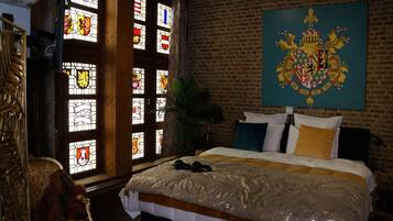 Een slaapkamer met een groot bed, een houten hoofdbord, een bakstenen muur en glas-in-loodramen.
