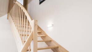 Un escalier en bois avec une rampe, une applique murale et un tableau encadré représentant un navire sur l’océan.