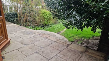 Eine gepflasterte Terrasse mit geschwungener Kante, umgeben von Grünpflanzen und einer Backsteinmauer.