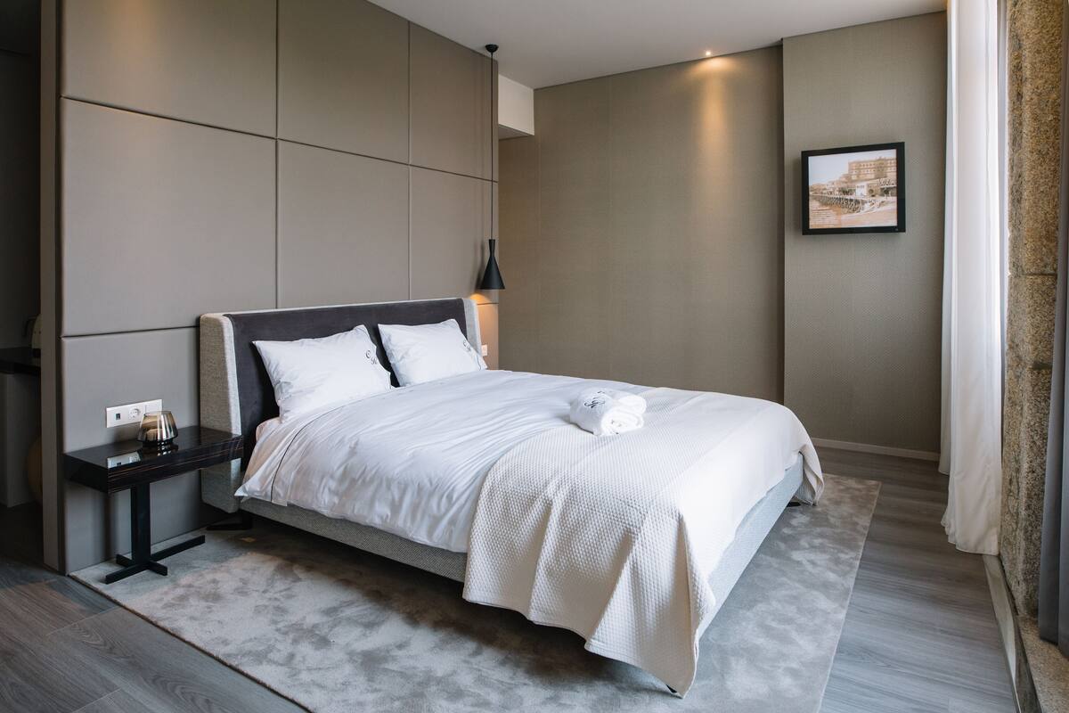 A modern hotel room with a large bed, a bedside table, a lamp, and a framed picture on the wall.