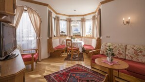 A cozy living room with a wooden bench, a sofa, a dining table with chairs, and a TV. - Hotel Viktoria & Landhaus Joggl (Mayrhofen)