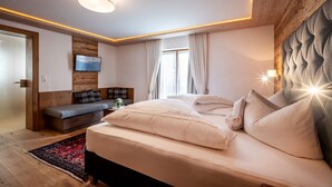A modern bedroom with a bed, a sofa, a TV, and a window with curtains. - Hotel Viktoria & Landhaus Joggl (Mayrhofen)