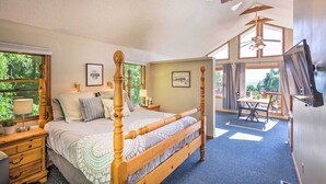 Een ruime slaapkamer met een groot bed, een houten hoofdbord, een plafondventilator en uitzicht op de omgeving door grote ramen.