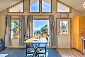 Une pièce comprenant une table à manger, des chaises, une horloge et une vue sur une maison par la fenêtre.