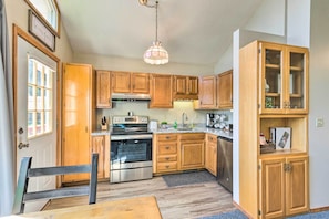 A kitchen with wooden cabinets, stainless steel appliances, and a hanging light fixture. - Hendersonville 'Cantrell Cottage' - Smoky Mtn View (Hendersonville)