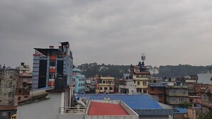 Paisagem urbana com diversos edifícios, incluindo uma construção imponente de vários andares com telhado vermelho e um prédio menor com telhado azul.