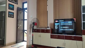 Quarto com televisão sobre um armário, um ventilador e uma porta que dá para o exterior.