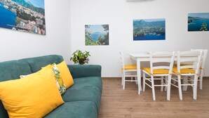 Een kamer met een groene bank, een eettafel met witte stoelen en drie ingelijste foto's aan de muur.