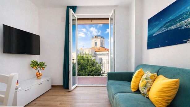 Een moderne woonkamer met een groene bank, een flatscreen televisie, een eethoek en een balkon met uitzicht op een gebouw en de zee.