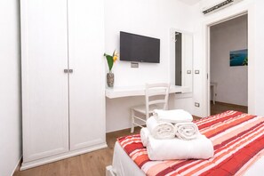 Una camera d'albergo con un letto, una scrivania, una sedia, una televisione e un armadio.