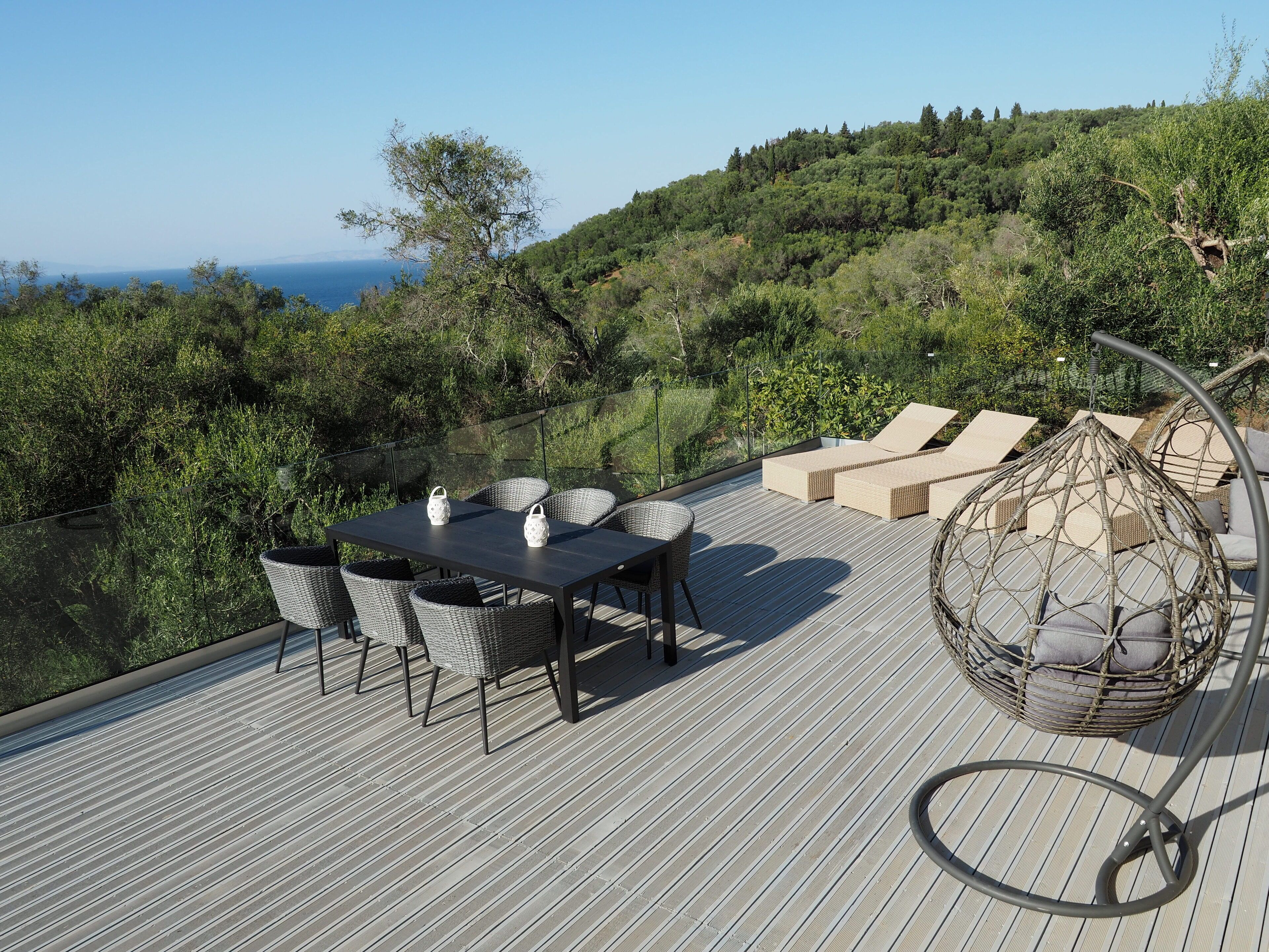 A deck with a table and chairs, a hanging chair, and a view of a forested hillside.