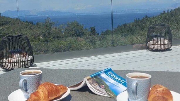 Ein Tisch mit zwei Croissants, zwei Kaffeetassen und einer Zeitschrift auf einer Terrasse mit Blick auf eine schöne Landschaft.