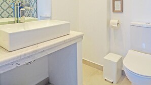 Ein modernes Badezimmer mit einem weißen Waschbecken, einem Spiegel, einer Toilette und einer kleinen Mülleimer.
