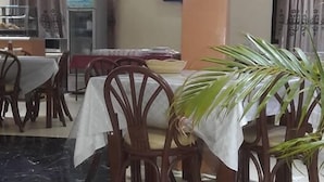 A dining area with wooden chairs and tables, a potted plant, and a television on the wall. - Twiggs Hotel (Bomet)