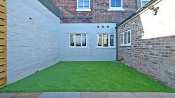 A small, enclosed courtyard with a green lawn, white brick walls, and a wooden fence.