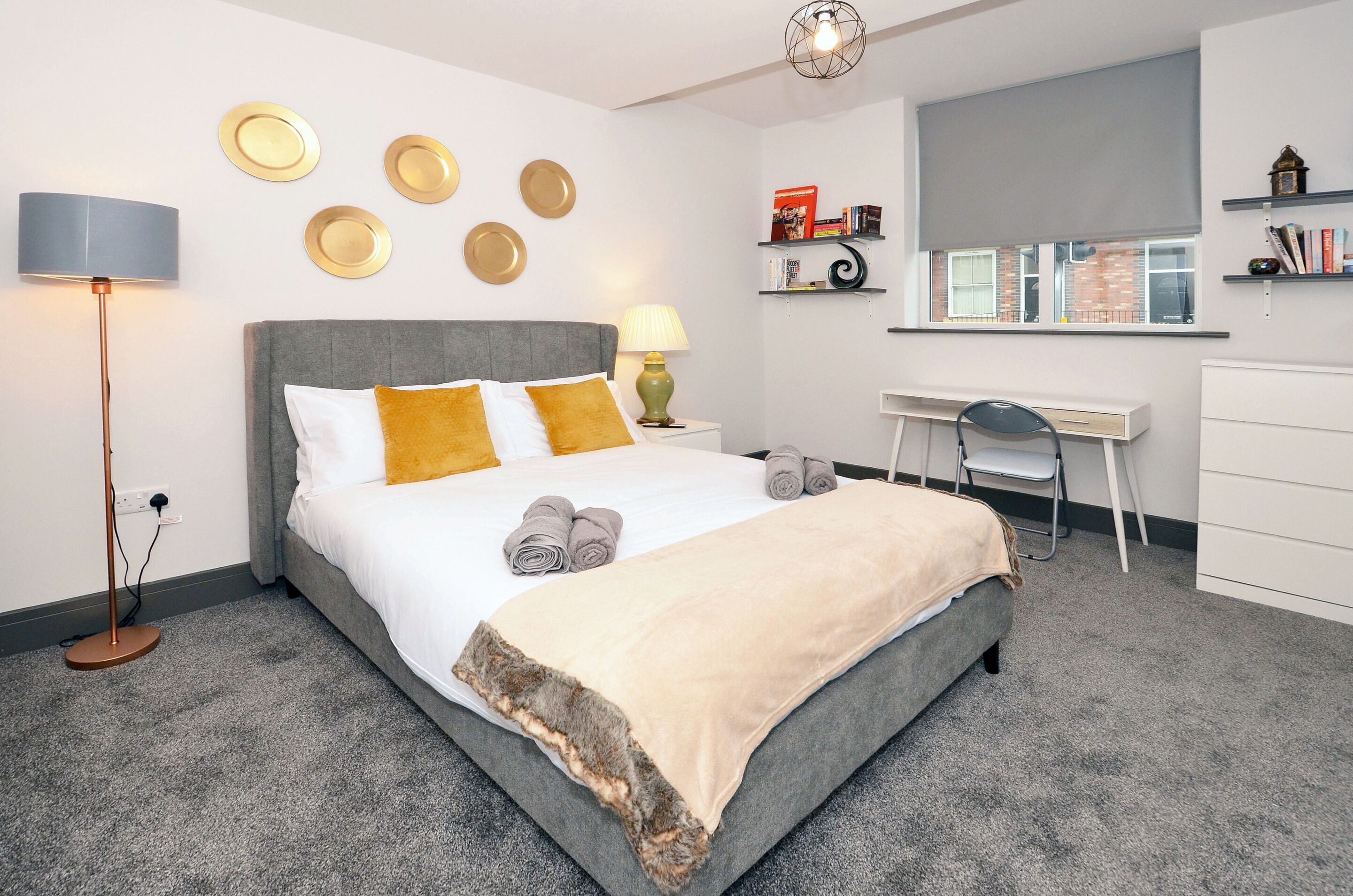 A modern bedroom with a bed, bedside lamps, a desk, and a chair.