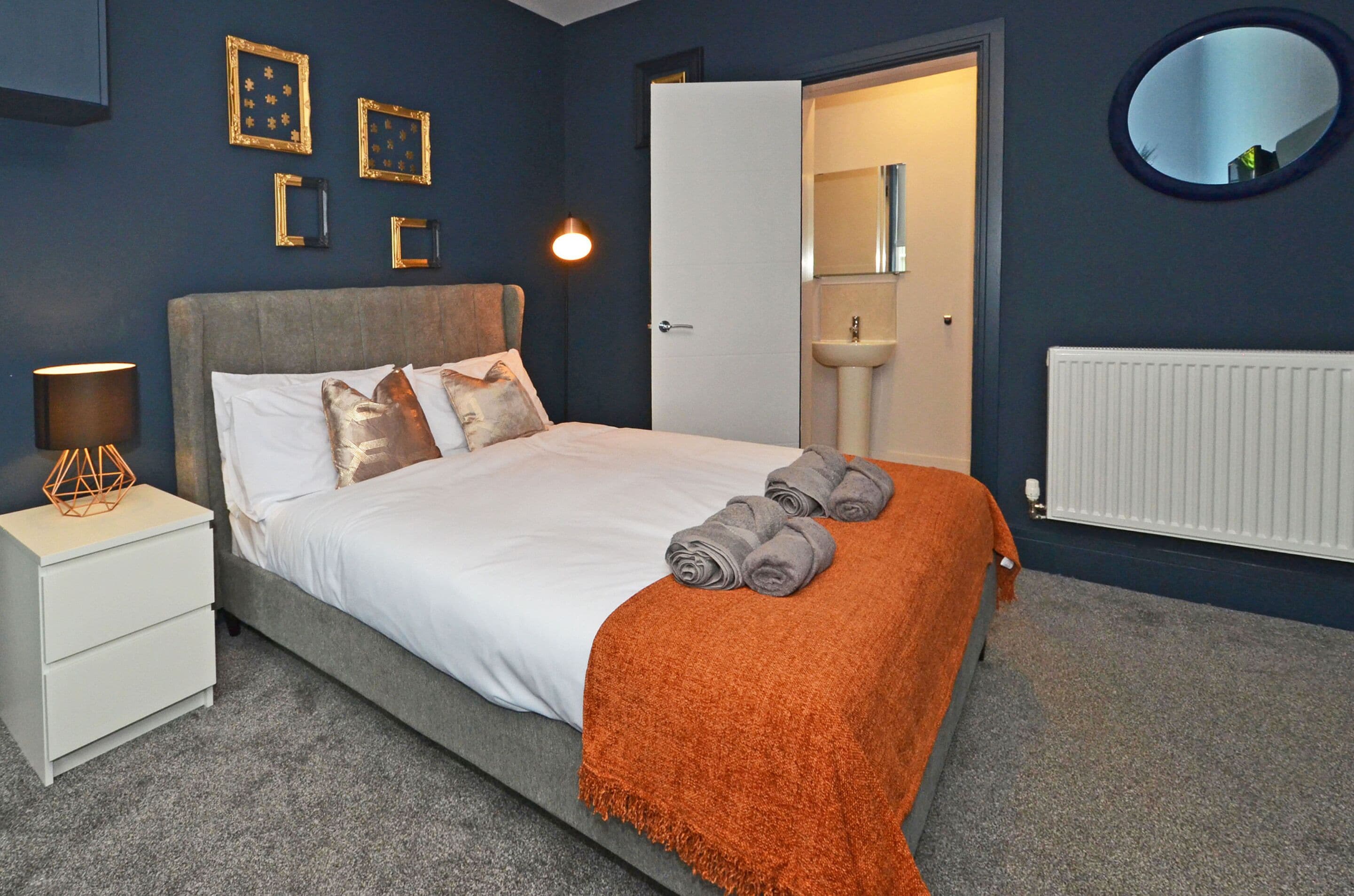 A bedroom with a bed, nightstand, and a bathroom visible through an open door.
