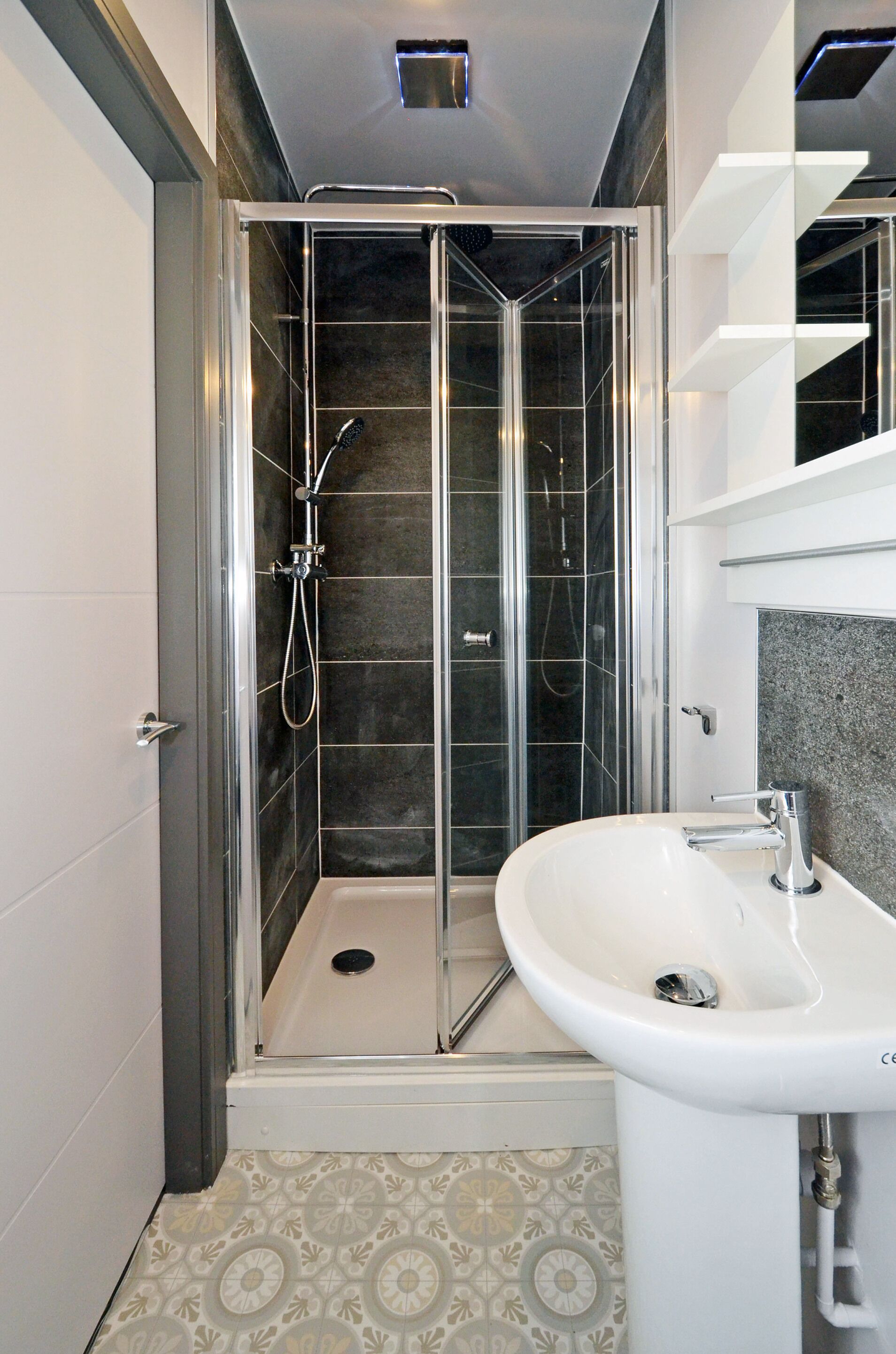 A modern bathroom with a glass-enclosed shower, a white sink, and patterned floor tiles.
