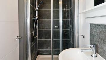 A modern bathroom with a glass-enclosed shower, a white sink, and patterned floor tiles.