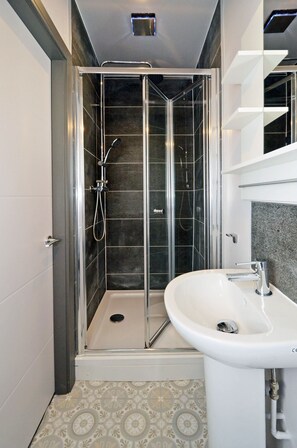 A modern bathroom with a glass-enclosed shower, a white sink, and patterned floor tiles.