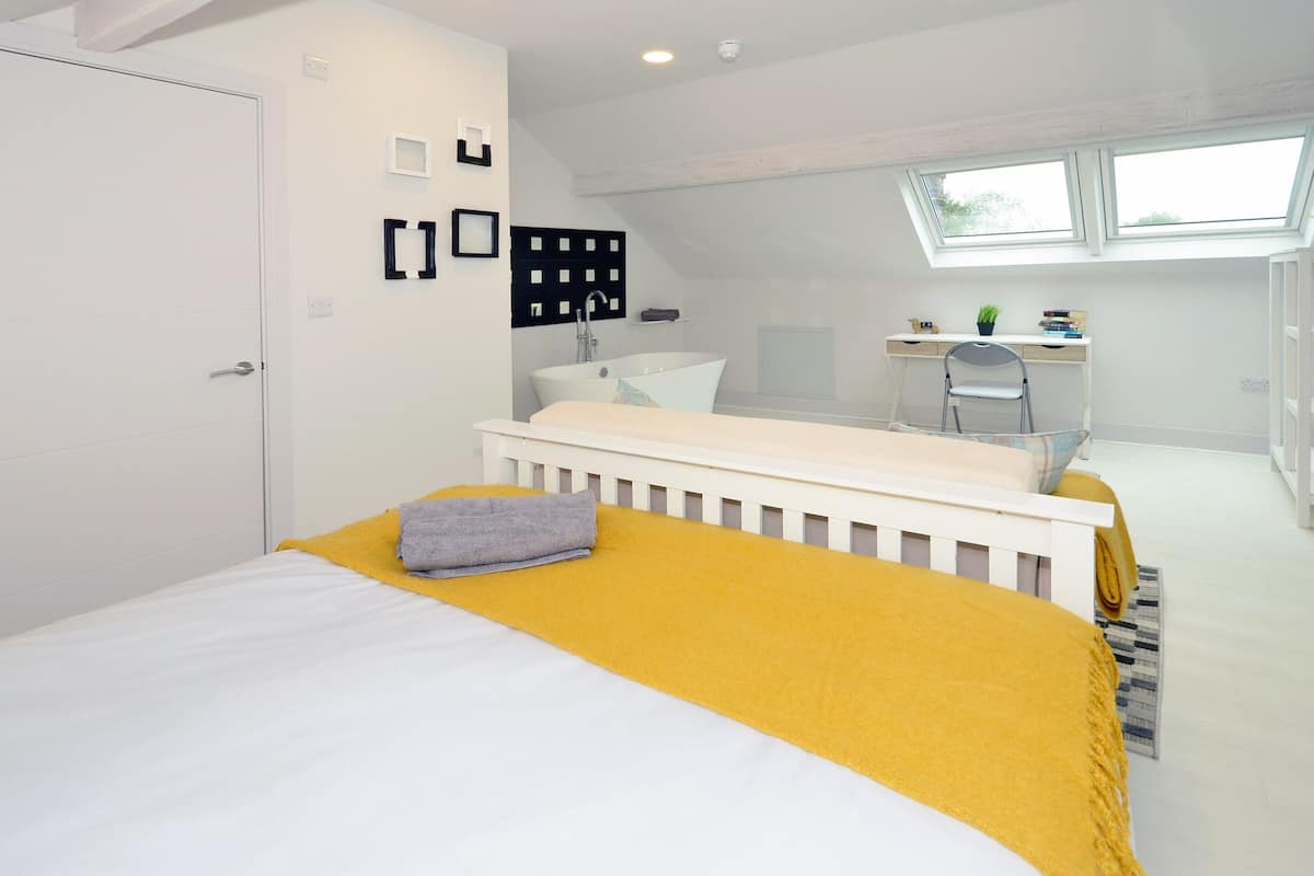 A bedroom with a bed, a desk, a chair, a window, and a white door.