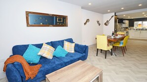 Un salon avec un canapé bleu, une table basse en bois et un coin repas comprenant une table et des chaises jaunes.