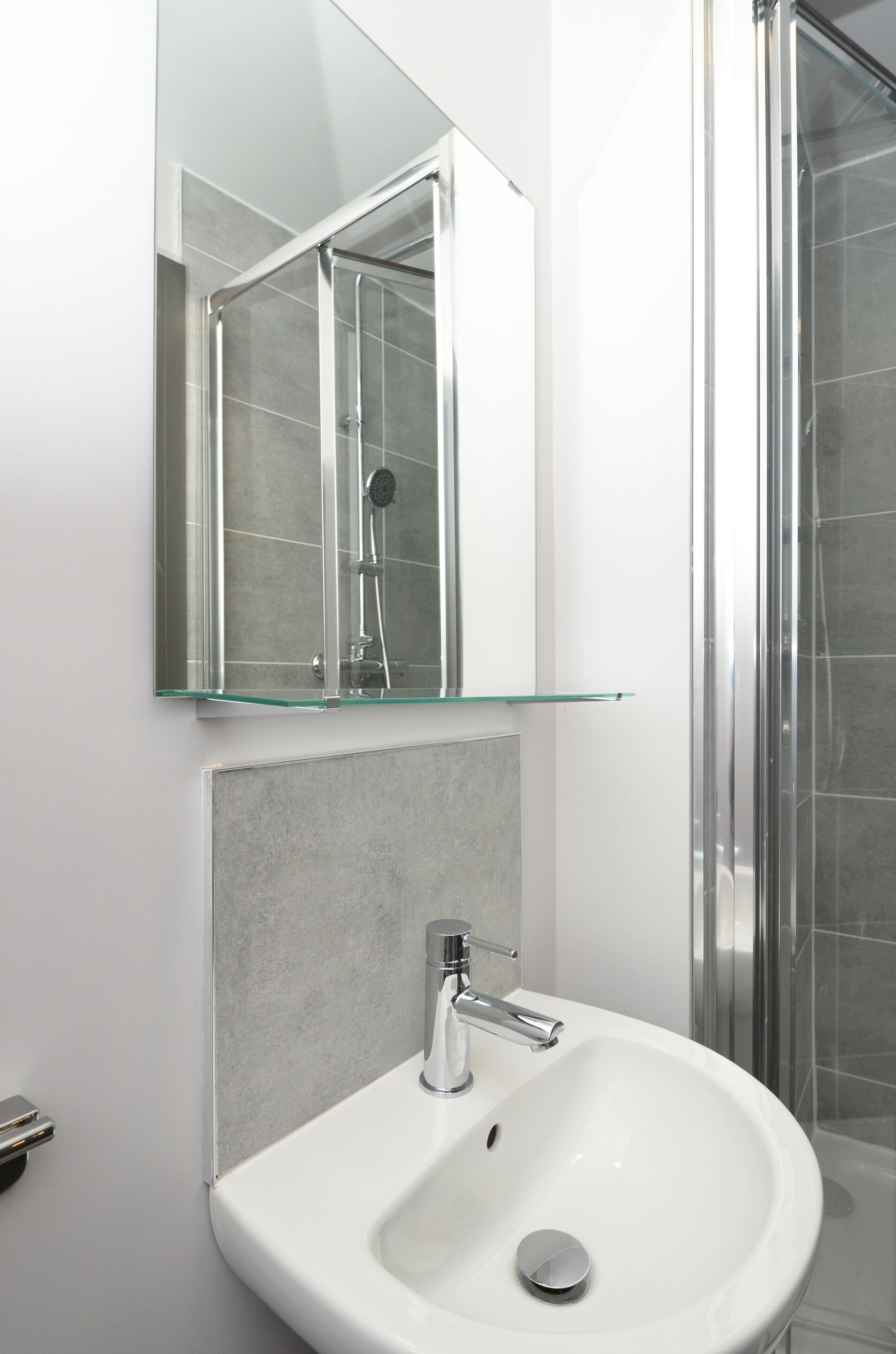 A bathroom with a glass shower enclosure, a white sink, and a mirror above the sink.