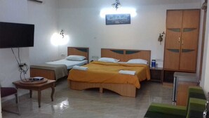 A hotel room with two single beds and a larger bed, a television mounted on the wall, a wooden wardrobe, and a small table with a book. - Hotel Rajdhani (Mawal)