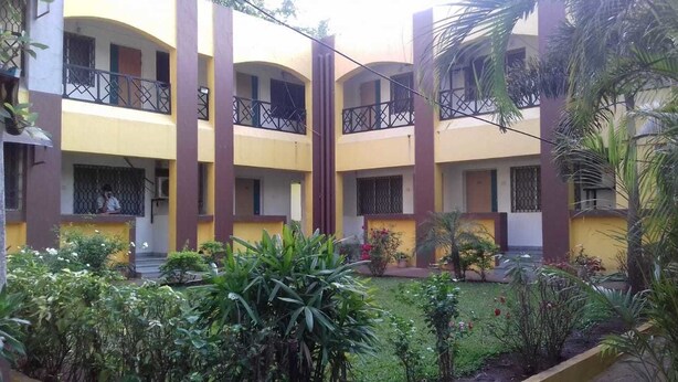 A multi-story building with balconies, surrounded by a garden with various plants and flowers. - Hotel Rajdhani (Mawal)