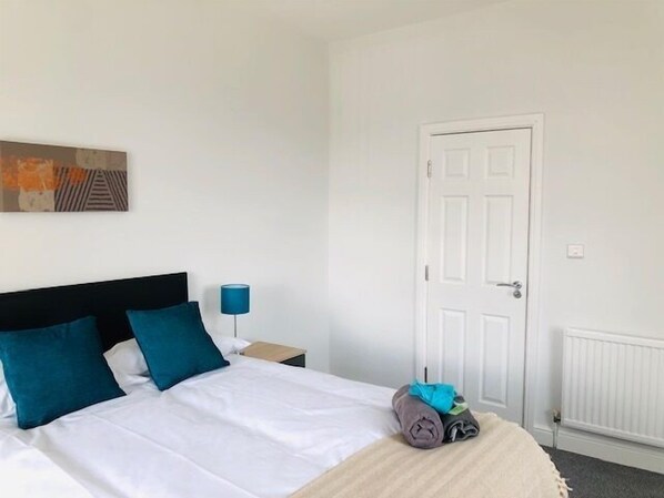 A hotel room with a bed, a nightstand, a lamp, a door, and a radiator. - Townhouse @ 51 Balfour St -stoke (Stoke-on-Trent)
