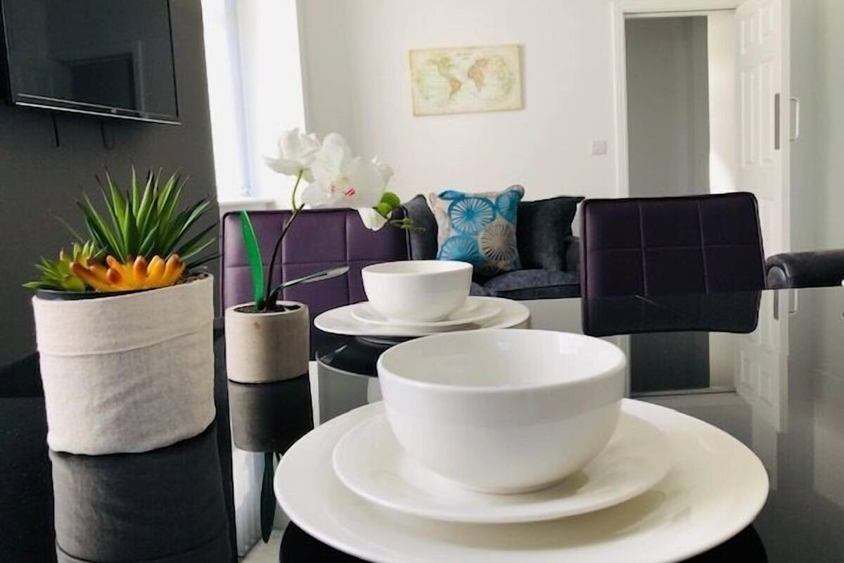 A modern kitchen with a dining area, featuring a TV, a world map, and a sofa with decorative pillows.