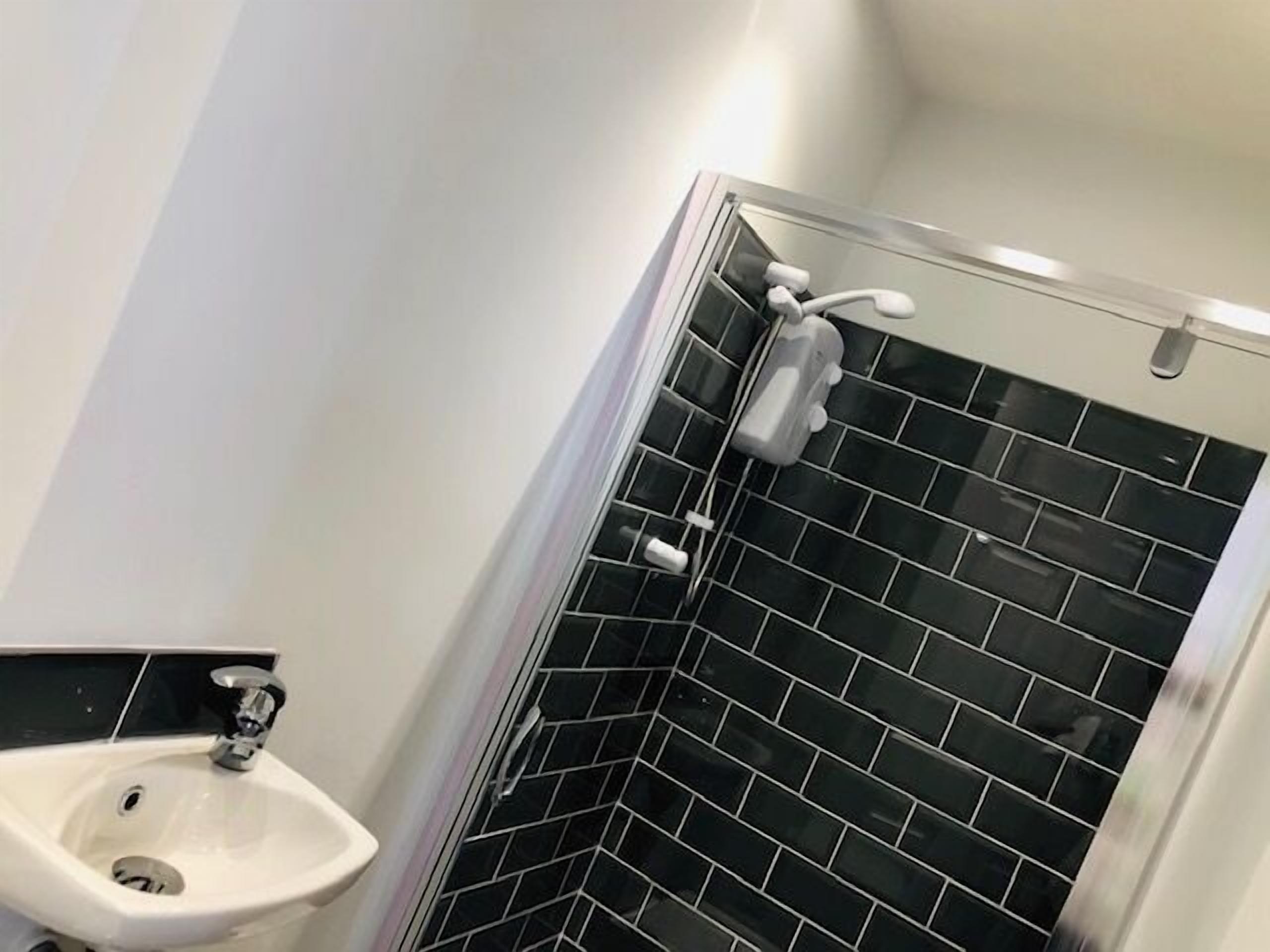 A bathroom with a white sink, black tiled shower walls, and a glass shower enclosure.